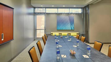 Un salón de conferencias con una larga mesa, sillas, botellas de agua y una pantalla para proyector.
