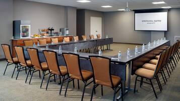 A conference room with a long table, chairs, a refrigerator with beverages, and a screen displaying 'SPRINGHILL SUITES® MARRIOTT'.