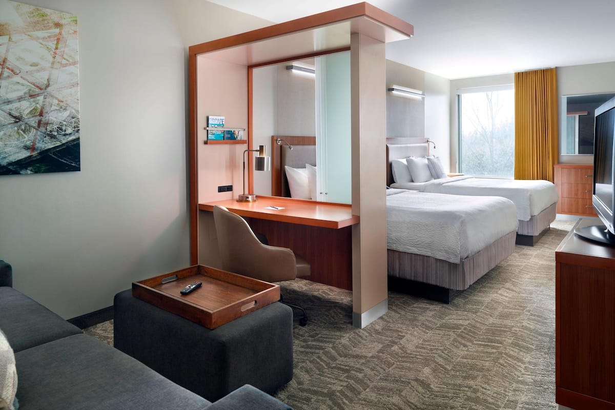 A hotel room with a desk, two beds, a sofa, a TV, and a large window.