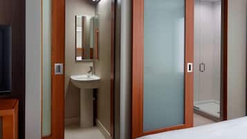 Habitación de hotel con armario de madera, lavamanos blanco y cabina de ducha de cristal.