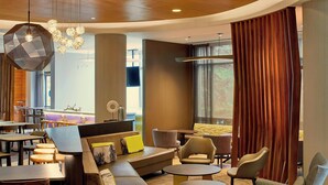 A modern hotel lobby with a seating area, tables, and a large window with curtains.