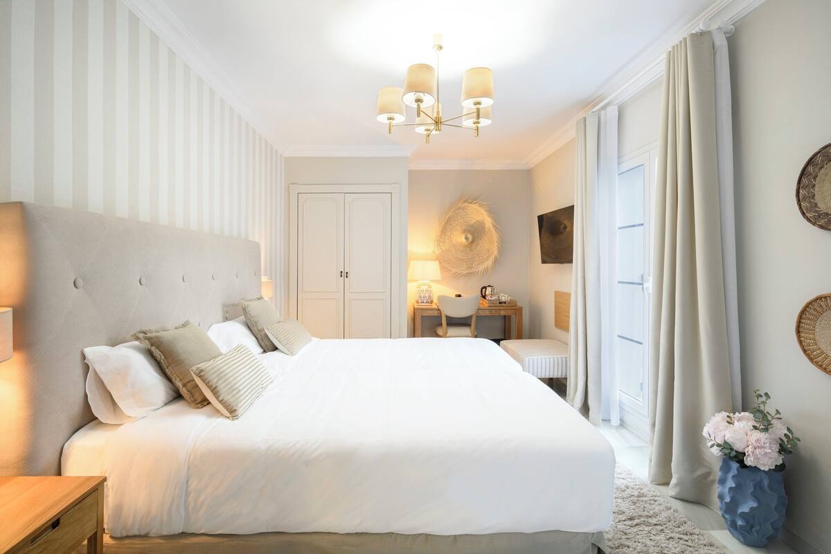 A bedroom with a large bed, a desk, a chair, and a decorative wall piece.