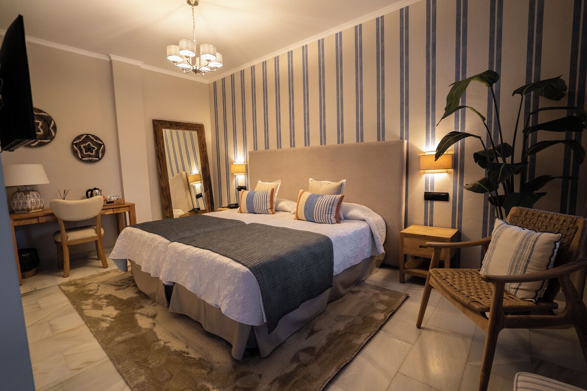A bedroom with a large bed, bedside tables, a chair, a mirror, and a plant.