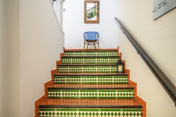 A staircase with green and brown tiles, a blue chair, and a sign indicating room numbers.