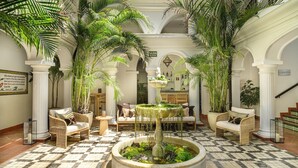A lobby with a checkered floor, white columns, wicker furniture, and a central fountain. - La Fonda Hotel (Benalmádena)