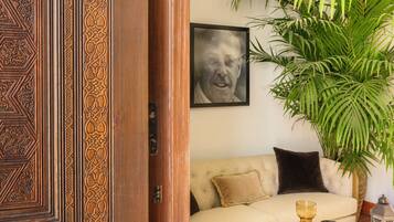A room with a wooden door, a beige sofa, a round wooden coffee table, a large potted plant, and a framed picture on the wall.