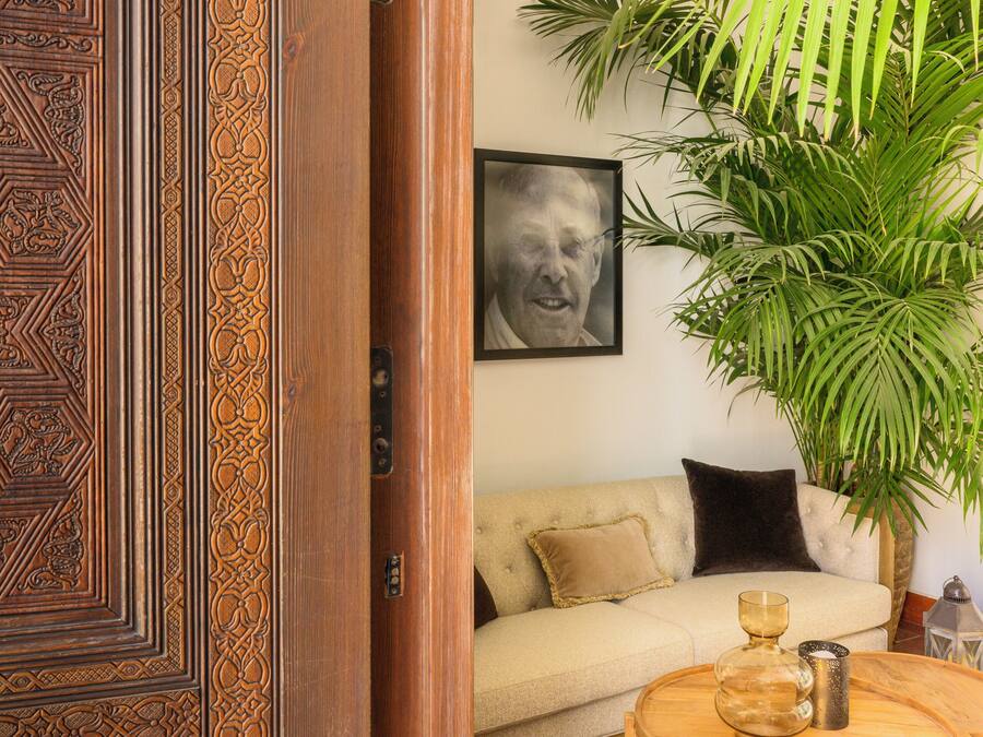 A room with a wooden door, a beige sofa, a round wooden coffee table, a large potted plant, and a framed picture on the wall.