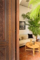 A room with a wooden door, a beige sofa, a round wooden coffee table, a large potted plant, and a framed picture on the wall.