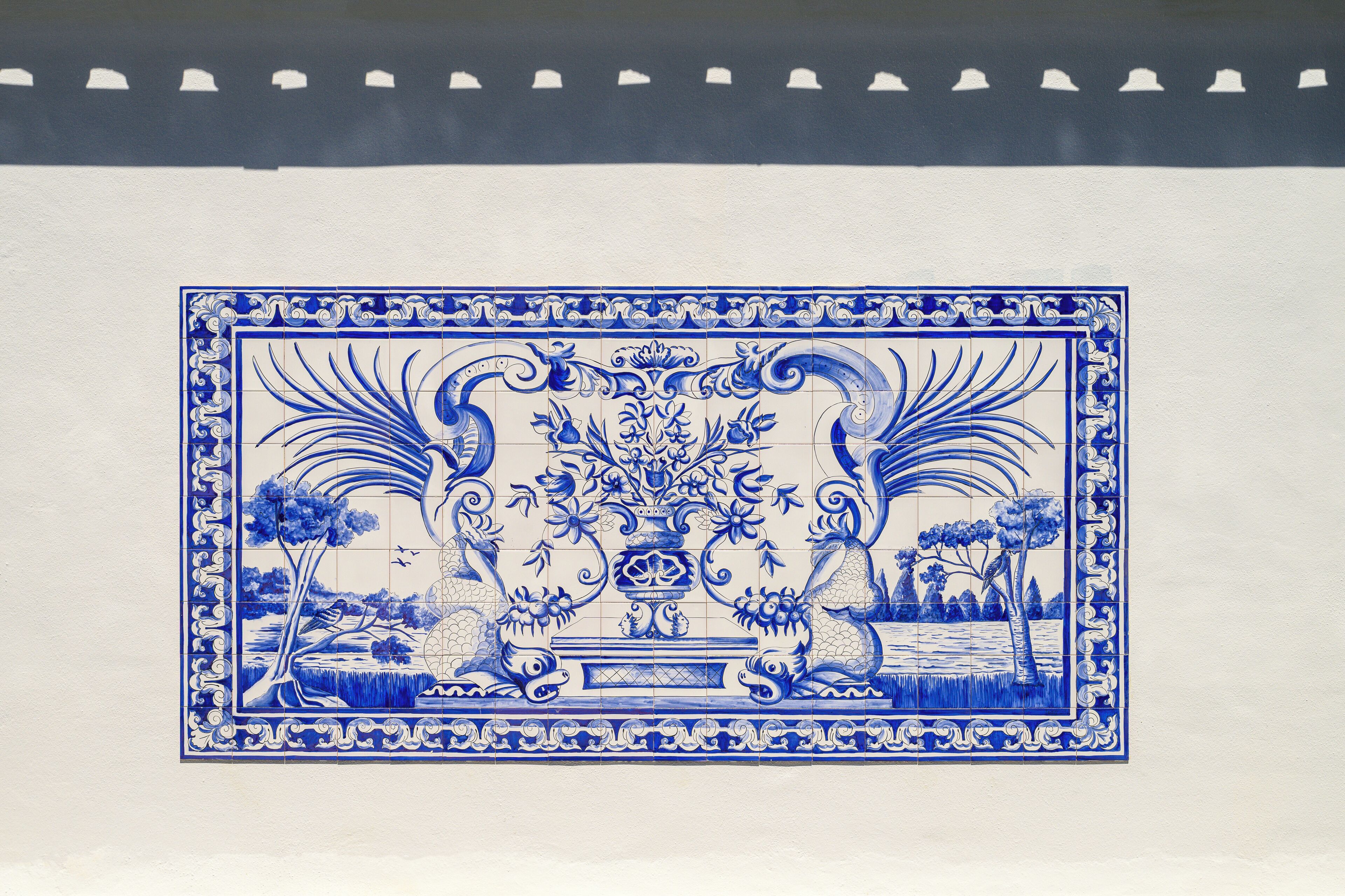 Eine blaue und weiße Keramikfliese mit traditionellem Dekor, zeigt Bäume, einen Teich und ein zentrales Ziertelement.