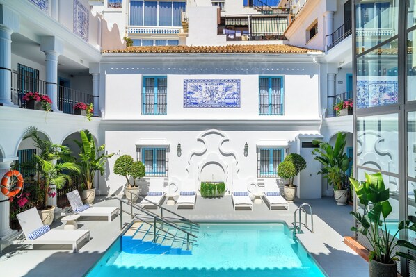 A rooftop pool area with lounge chairs, a swimming pool, and potted plants.
