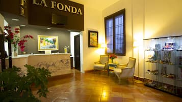 Un hall con una recepción, dos sillones, una vitrina de vidrio y un ventanal grande.