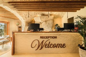 A reception desk with a 'RECEPTION Welcome' sign, two computer monitors, and a stone wall.