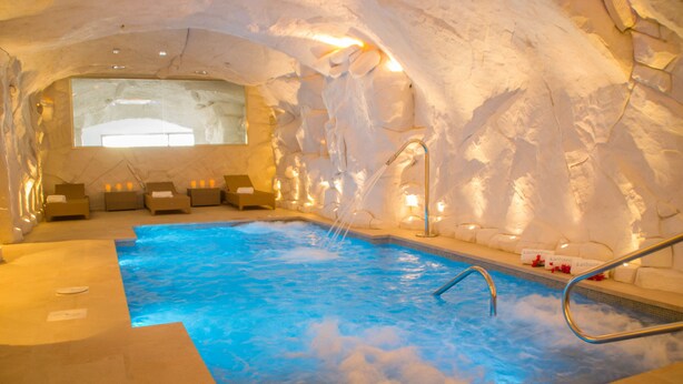 An indoor hot tub with a stone wall backdrop, a seating area with loungers, and a window providing natural light. - La Fonda Hotel (Benalmádena)