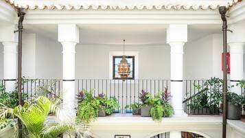 Un balcon couvert, orné de colonnes blanches, d’une lanterne suspendue et de plantes en pot.