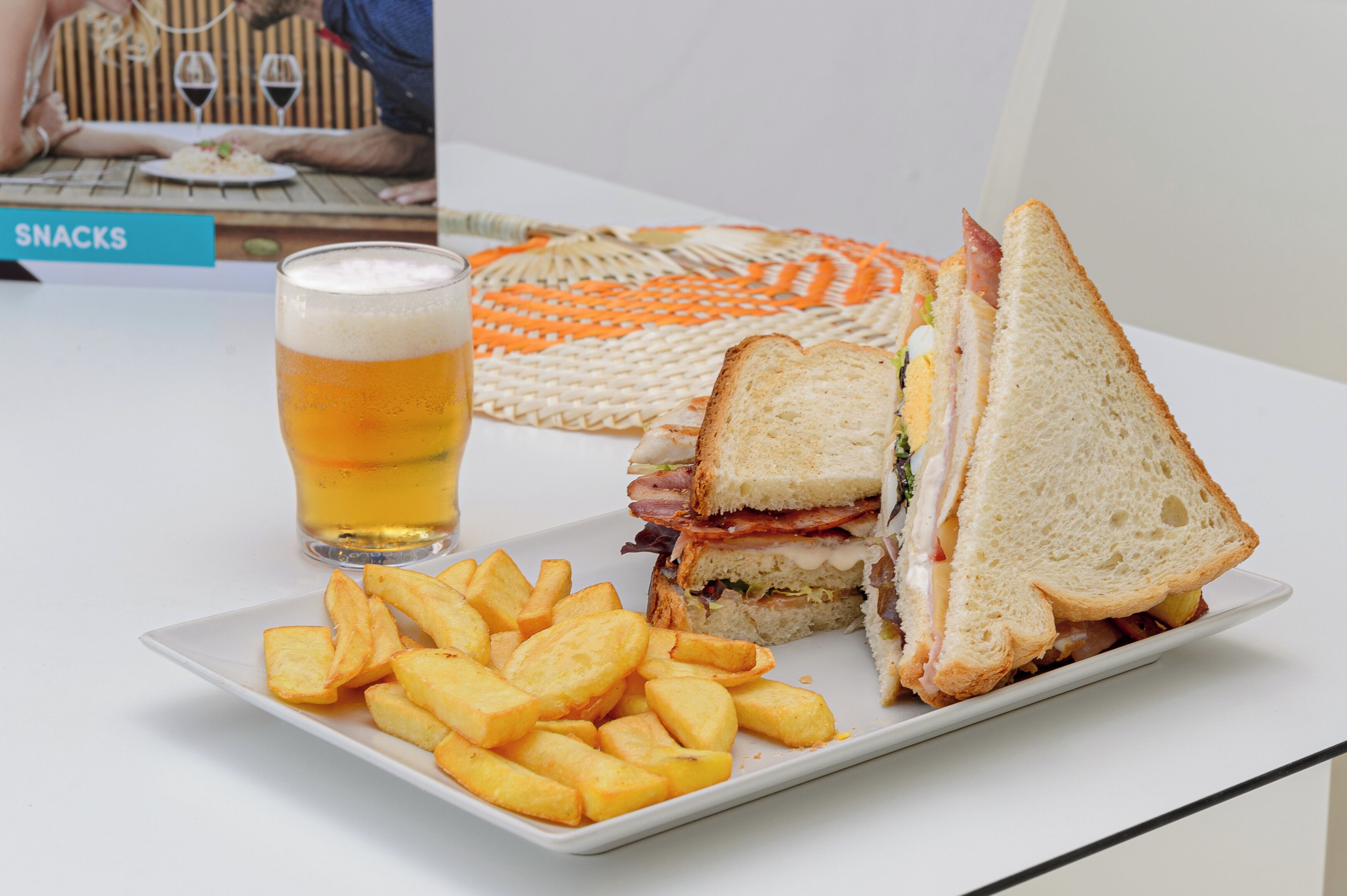 Un sándwich, una cerveza en un vaso y una porción de papas fritas sobre una mesa.