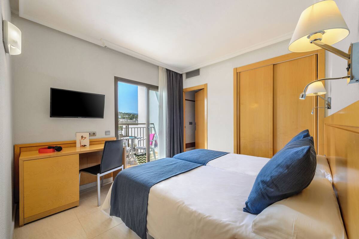 Habitación de hotel con cama, escritorio, silla, televisor y balcón con vistas.
