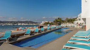 Un área junto a la piscina con sillones de descanso y vista al mar.