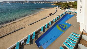 Un espace piscine avec des chaises longues et une vue sur la plage et la mer.