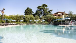 Una piscina nítida amb gandules i ombrelles, envoltada d'arbres i un edifici.