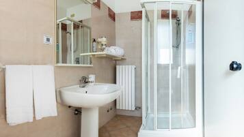 Un baño con lavamanos, espejo, toallero, cabina de ducha y retrete.