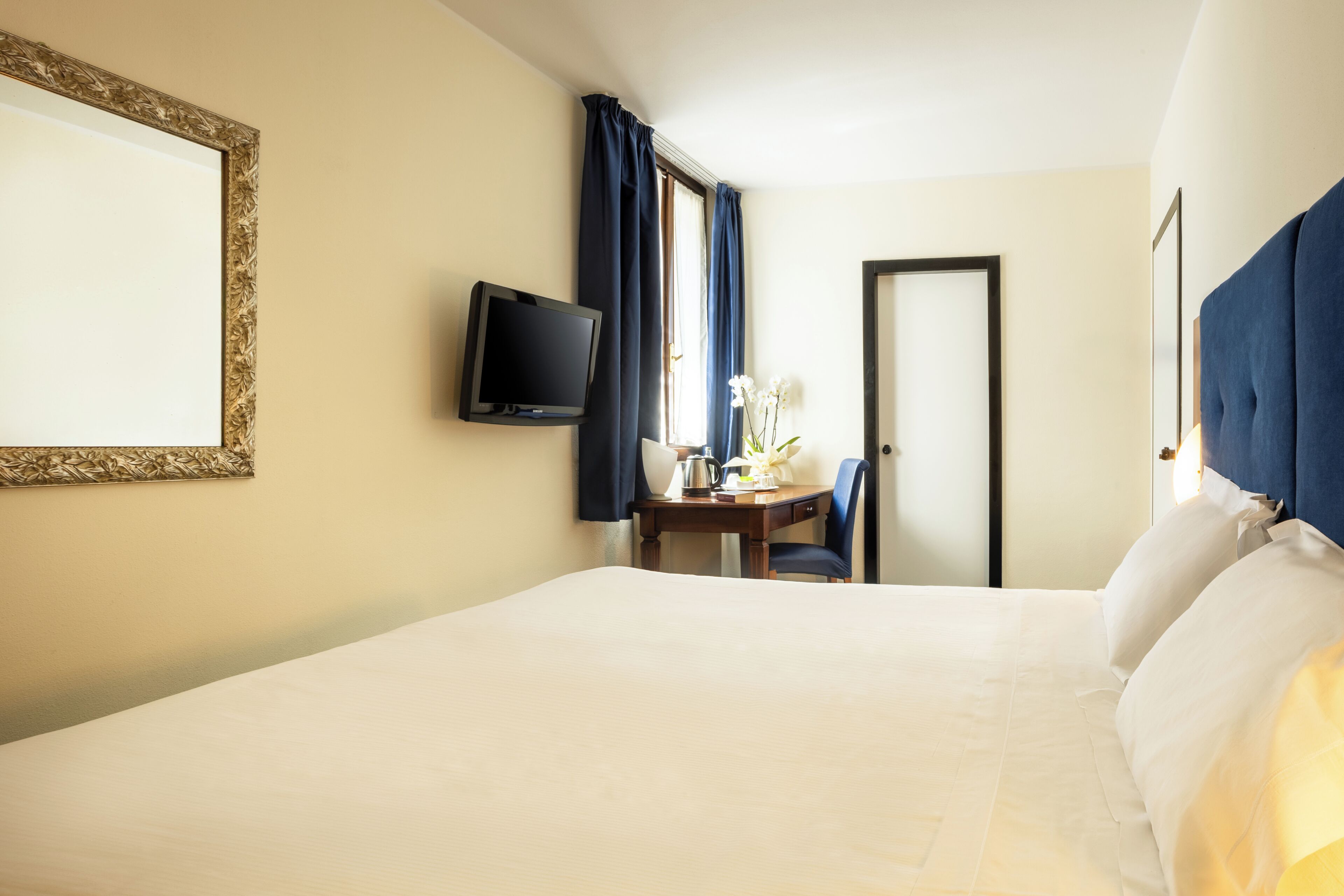 A hotel room with a bed, a desk with a chair, a television, and a door.