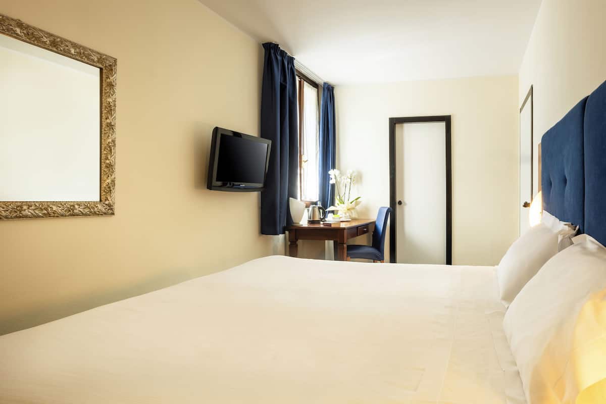 A hotel room with a bed, a desk with a chair, a television, and a door.