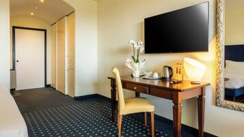 Habitación de hotel con cama, escritorio con silla, televisión, espejo y alfombra estampada.