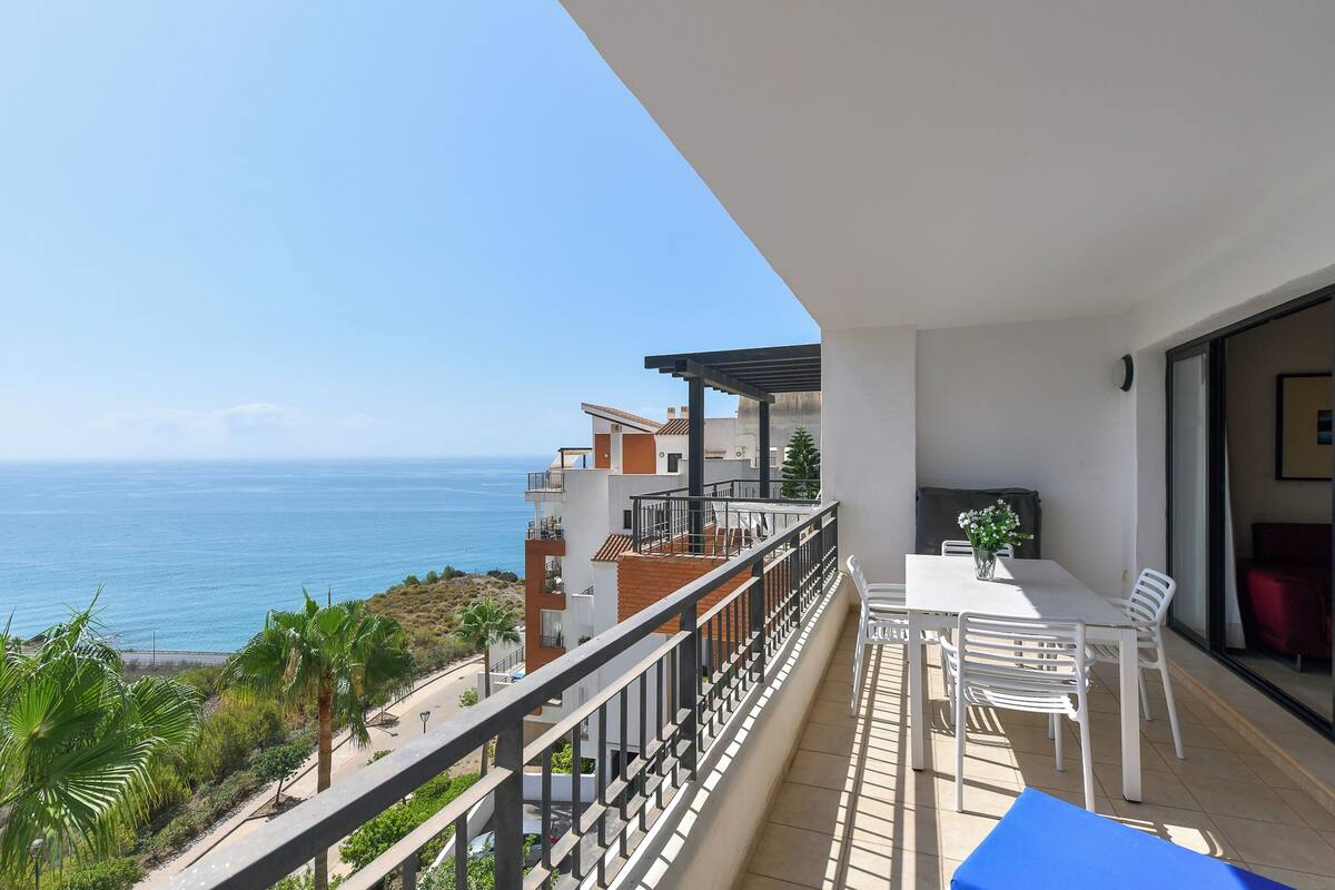 Un balcon avec vue sur la mer, un coin repas avec des chaises et une table, et un canapé rouge.