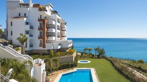 A modern multi-story building with a swimming pool, a well-maintained lawn, and a view of the sea. - Olée Nerja Holiday Rentals By Fuerte Group (Torrox)