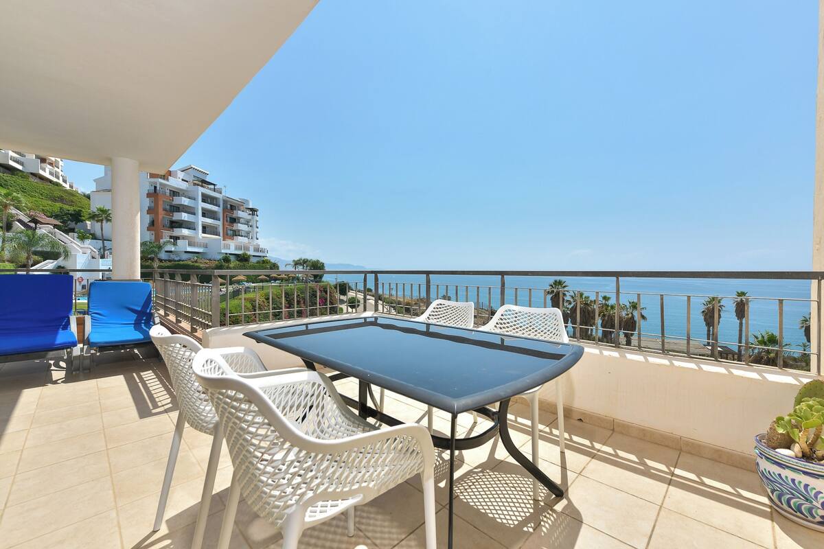 Un balcon avec une table et des chaises, un pot de fleurs et une vue sur la mer et les bâtiments.