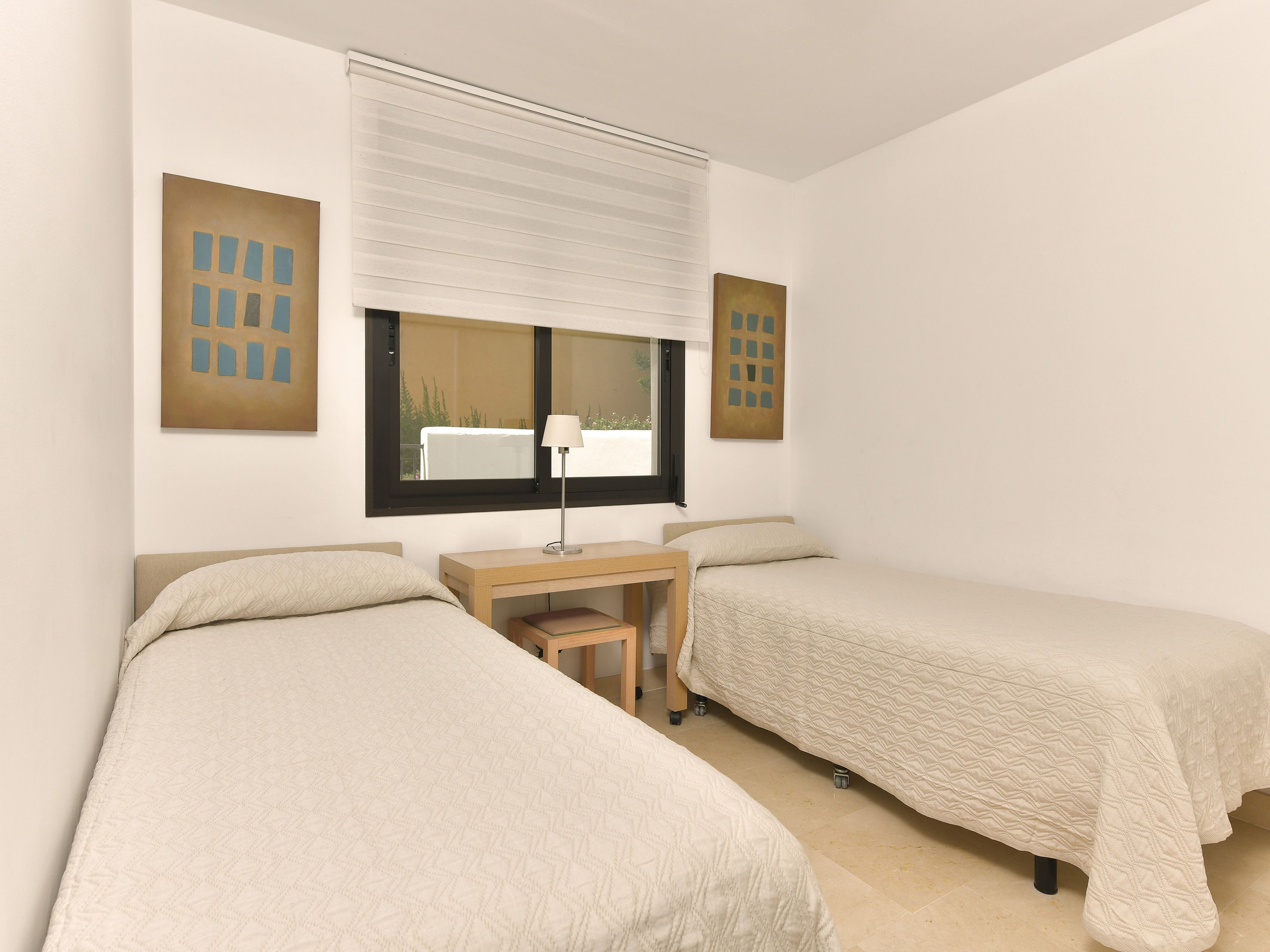 Una habitación con dos camas, un escritorio y una ventana con persianas.