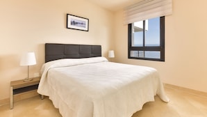 Une chambre à coucher avec un lit, une table de chevet, une lampe, un tableau au mur et une fenêtre donnant sur un paysage.