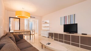 A modern living room with a sofa, a coffee table, a TV, and a dining area with chairs and a table. - Olée Nerja Holiday Rentals By Fuerte Group (Torrox)