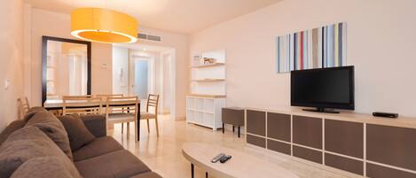 A modern living room with a sofa, a coffee table, a TV, and a dining area with chairs and a table.