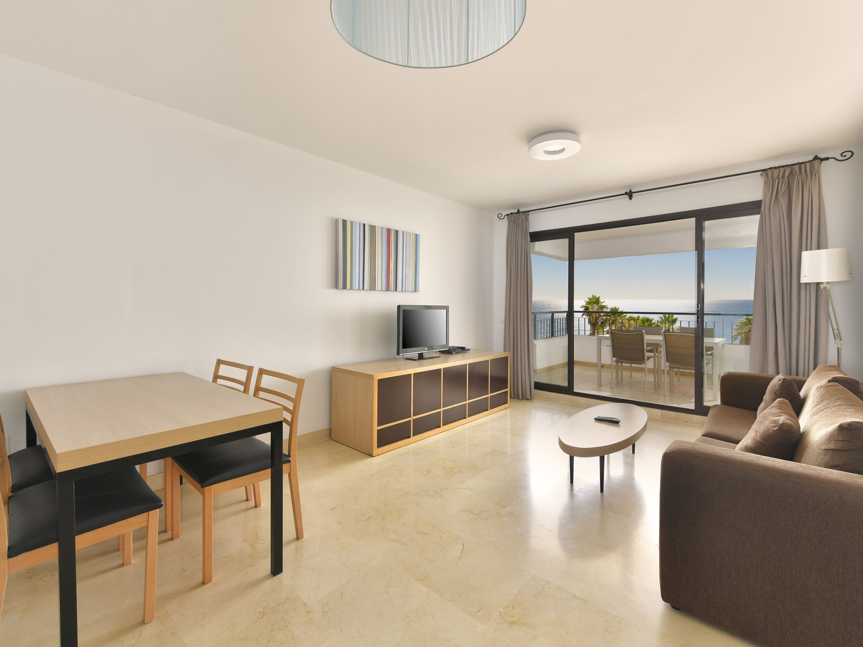A modern hotel room with a balcony, a dining area, and a seating area.