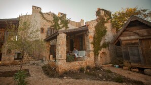 Un bâtiment rustique en pierre, doté d’un porche couvert, d’un escalier en pierre et d’un petit jardin.