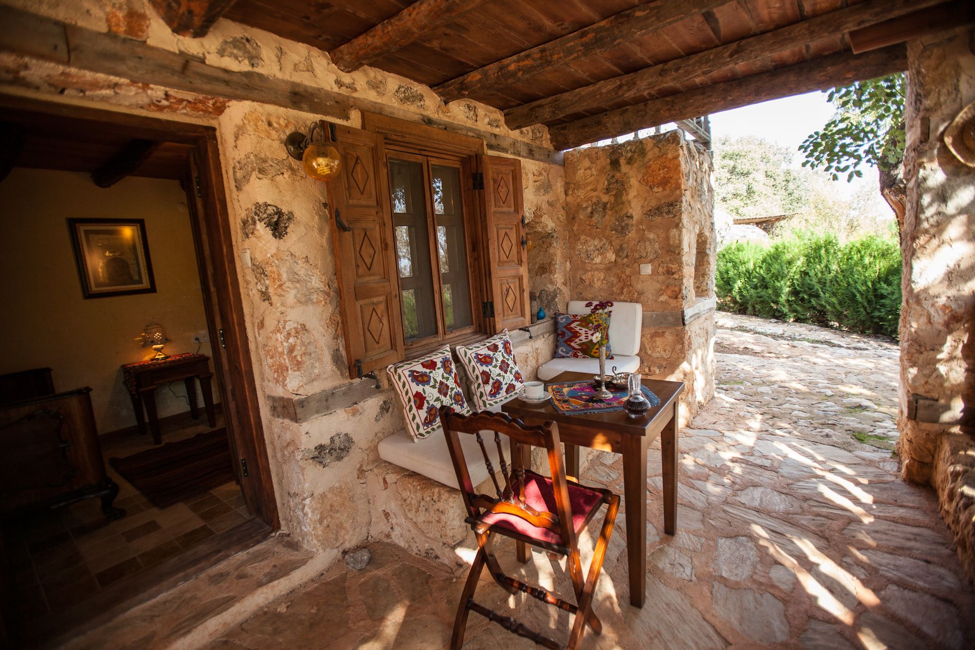 Un edificio rústico de piedra con puerta de madera, una pequeña mesa con una silla y un patio empedrado.