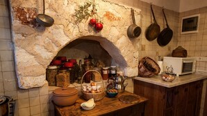 Une cuisine rustique avec une cheminée en pierre en forme d’arc, des armoires en bois et divers ustensiles de cuisine et bocaux.
