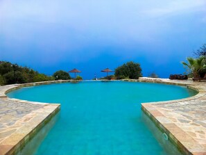 A large, clear blue swimming pool with stone borders, surrounded by trees and umbrellas. - Hoyran Wedre Country Houses (Demre)