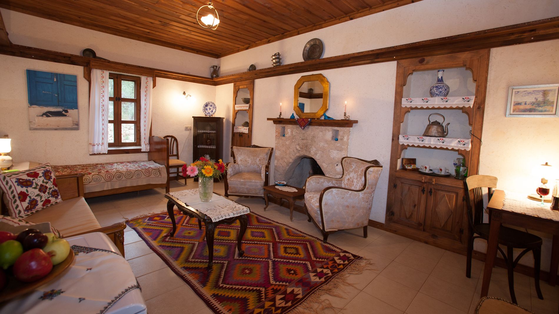 Una sala de estar acogedora con un sofá, sillones, una mesa de centro y una chimenea. Se observa un aparador de madera con objetos decorativos y un espejo sobre la chimenea.