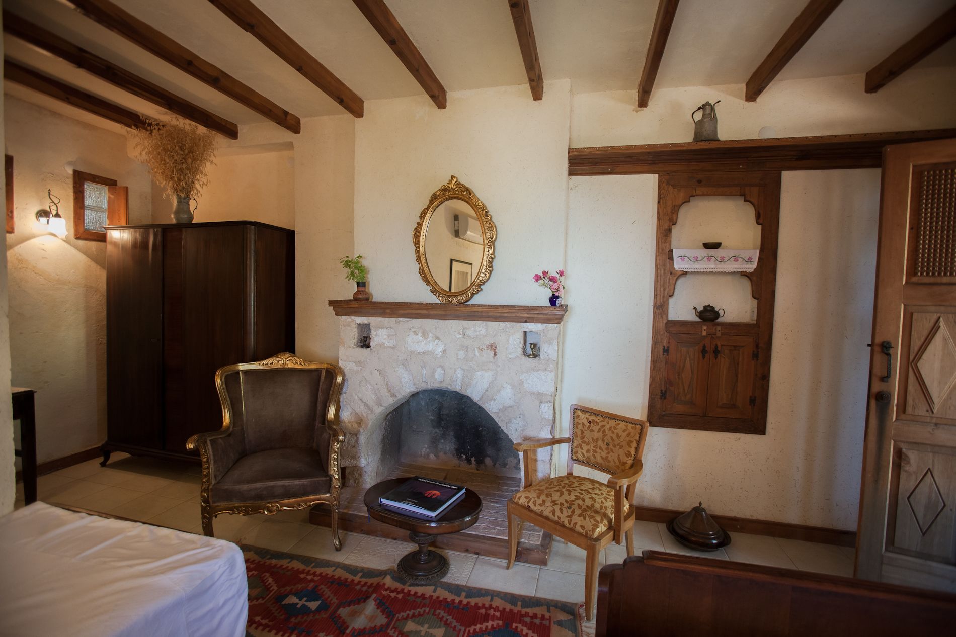 Una habitación acogedora con chimenea, dos sillones decorativos, un aparador de madera y un espejo en la pared.