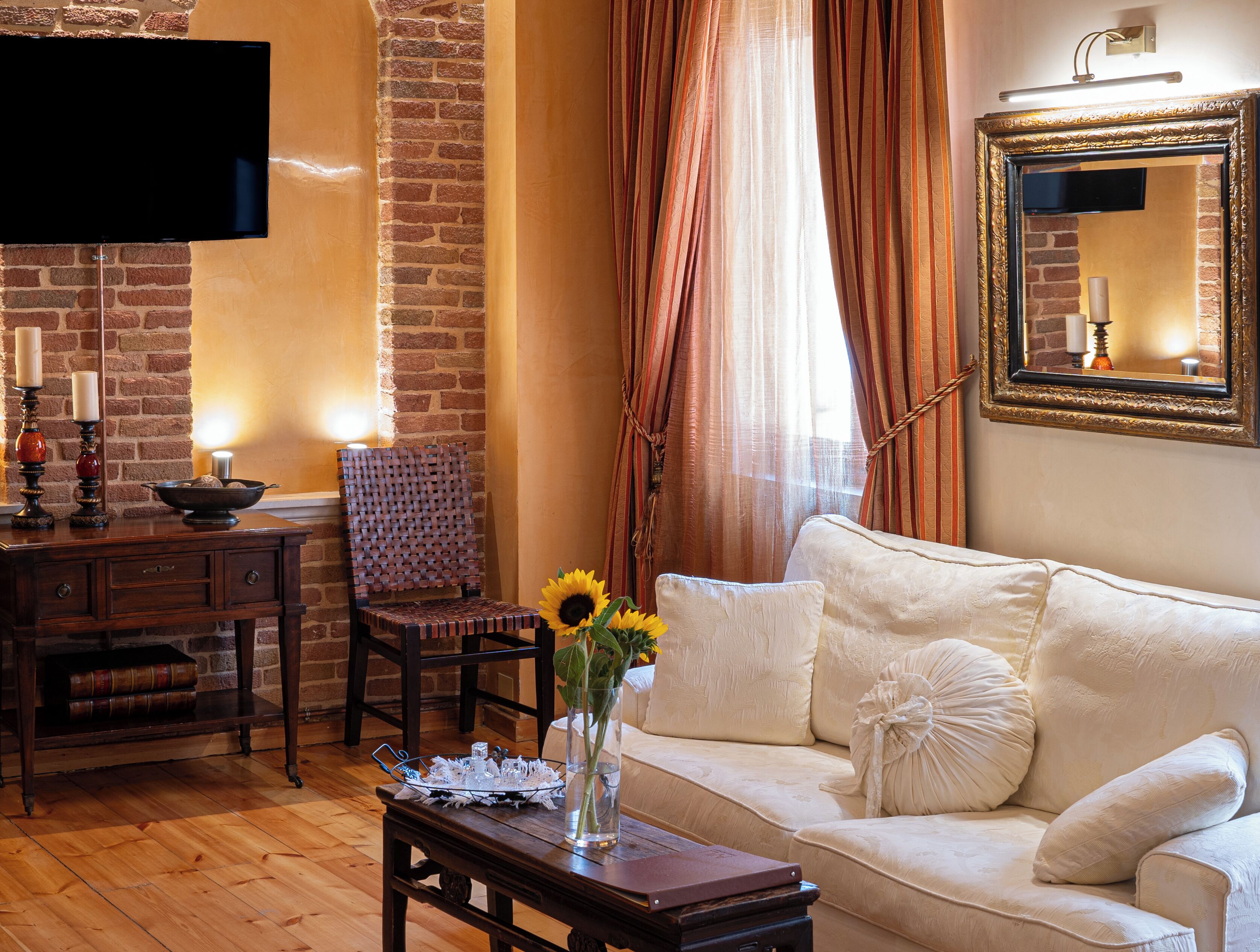 A living room with a brick wall, a flat-screen TV, a wooden table with a vase of sunflowers, a cushioned sofa, and a chair.