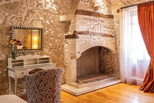 Lareira de pedra, toucador branco com espelho e poltrona estampada em um quarto com piso de madeira.