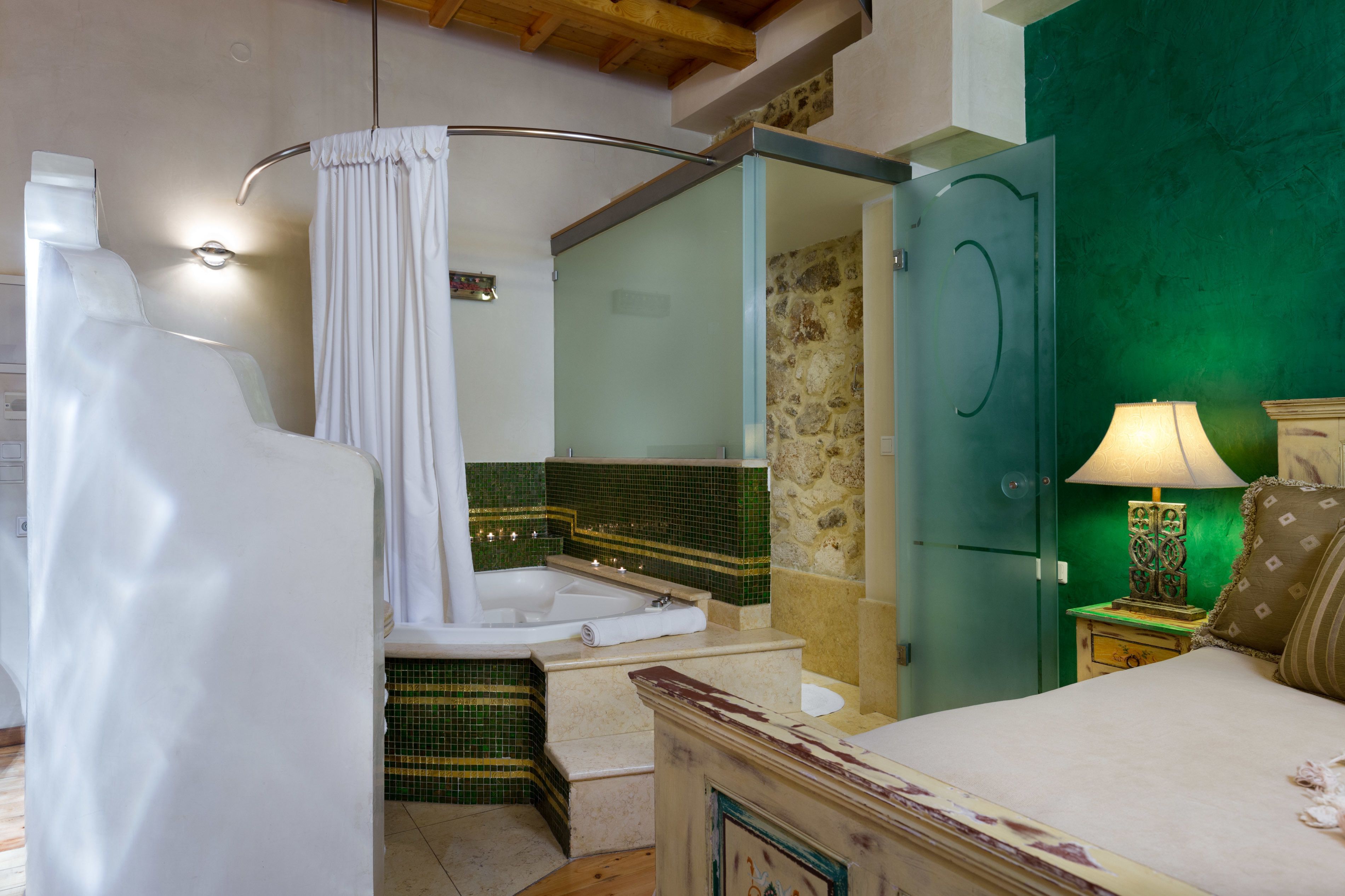 A bathroom with a bathtub, a shower curtain, a glass-enclosed shower, a green wall, and a bedside table with a lamp.