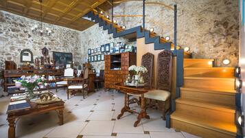 Una habitación con pared de piedra, escalera de madera y varios muebles, incluyendo una mesa con flores y un banco.