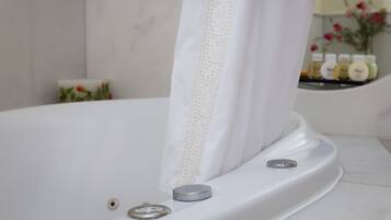 A white bathtub with a lace curtain, a control knob, and a small bottle of shampoo on the edge.