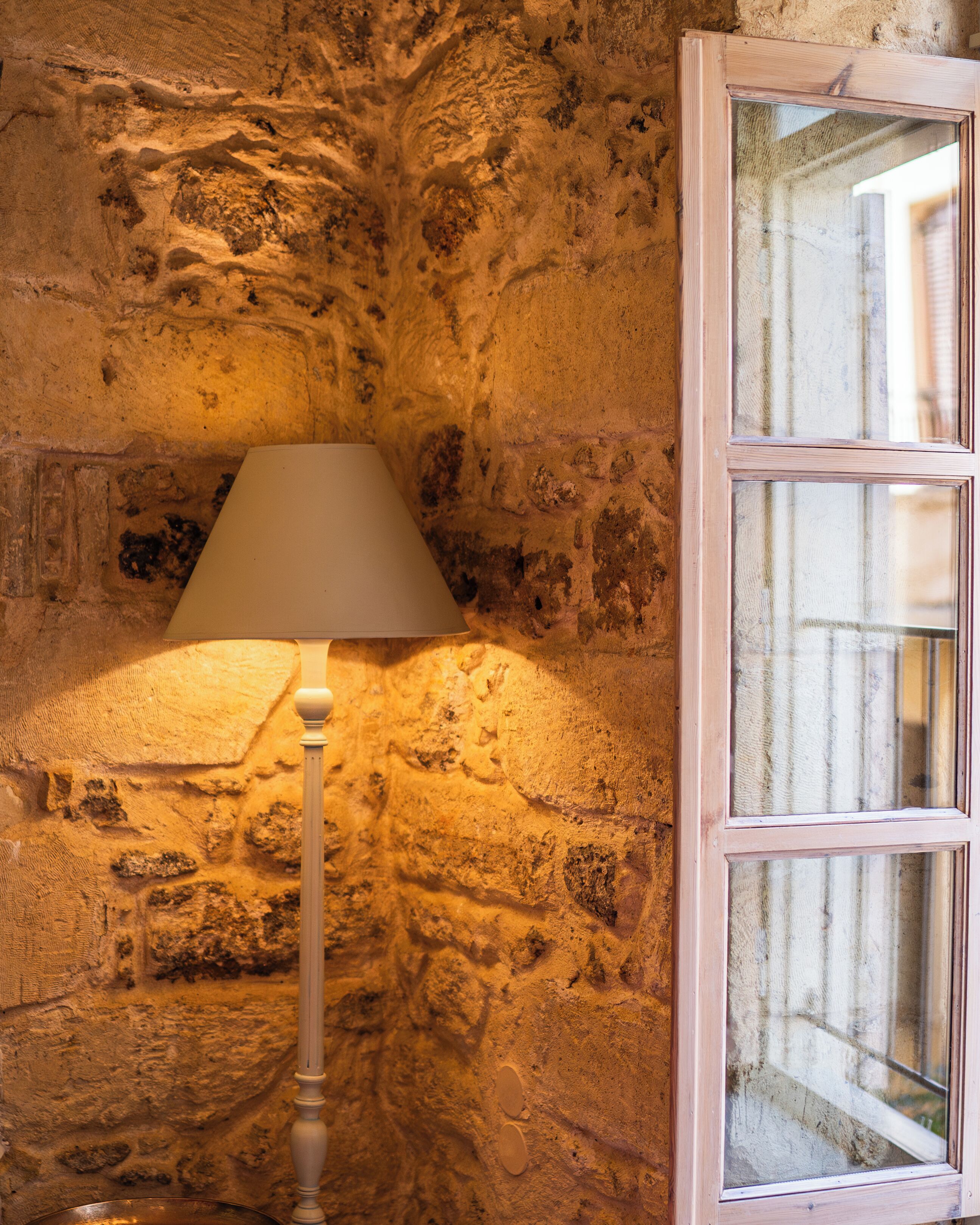 A lamp against a textured stone wall with a window.