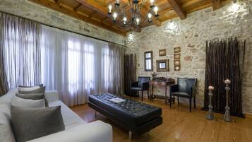 Una habitación con pared de piedra, techo de madera, un otomano negro, sofá blanco y una araña.
