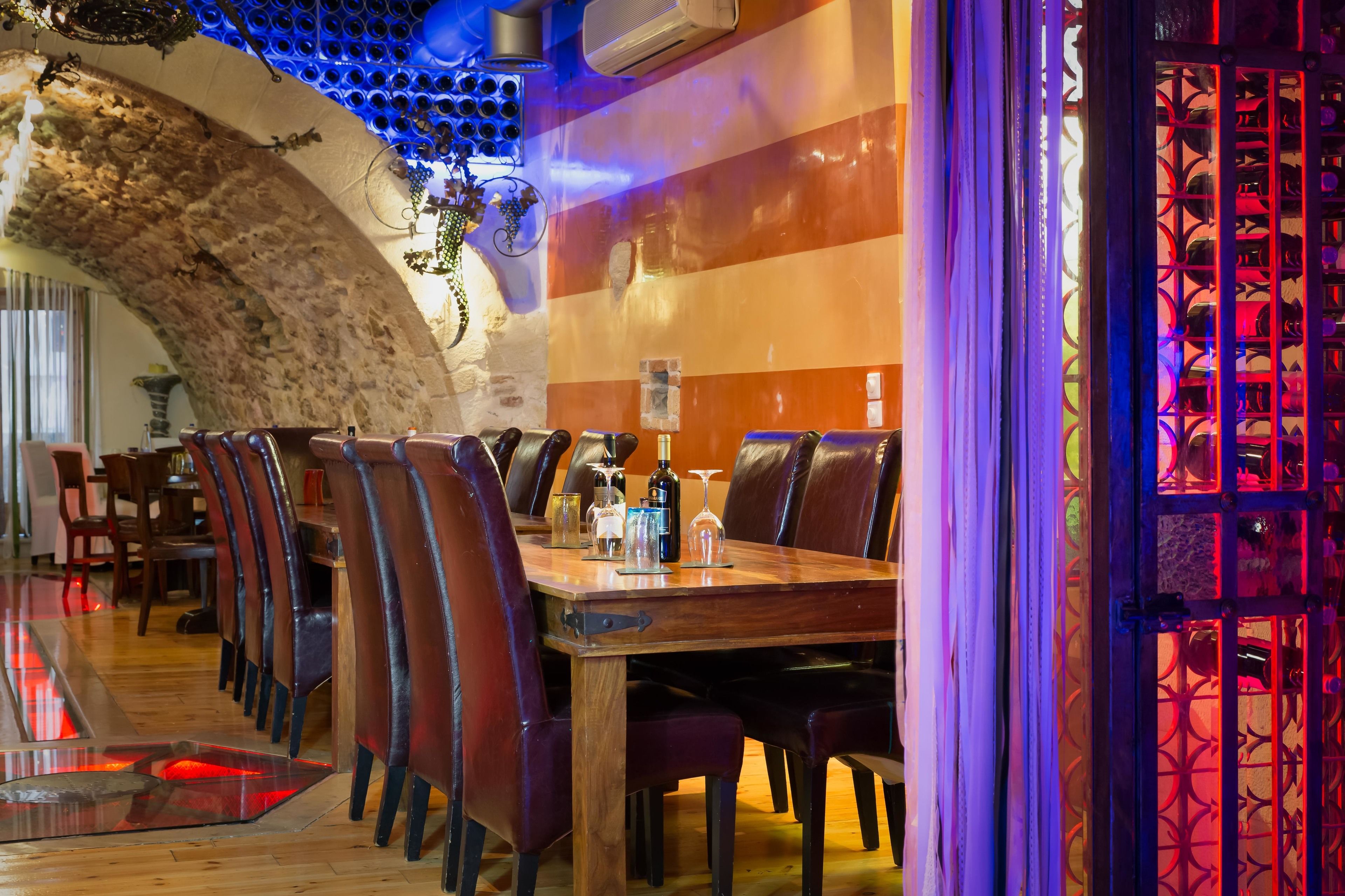 Un espace repas avec une longue table en bois, des chaises en cuir et un plafond décoratif doté d’un éclairage bleu.
