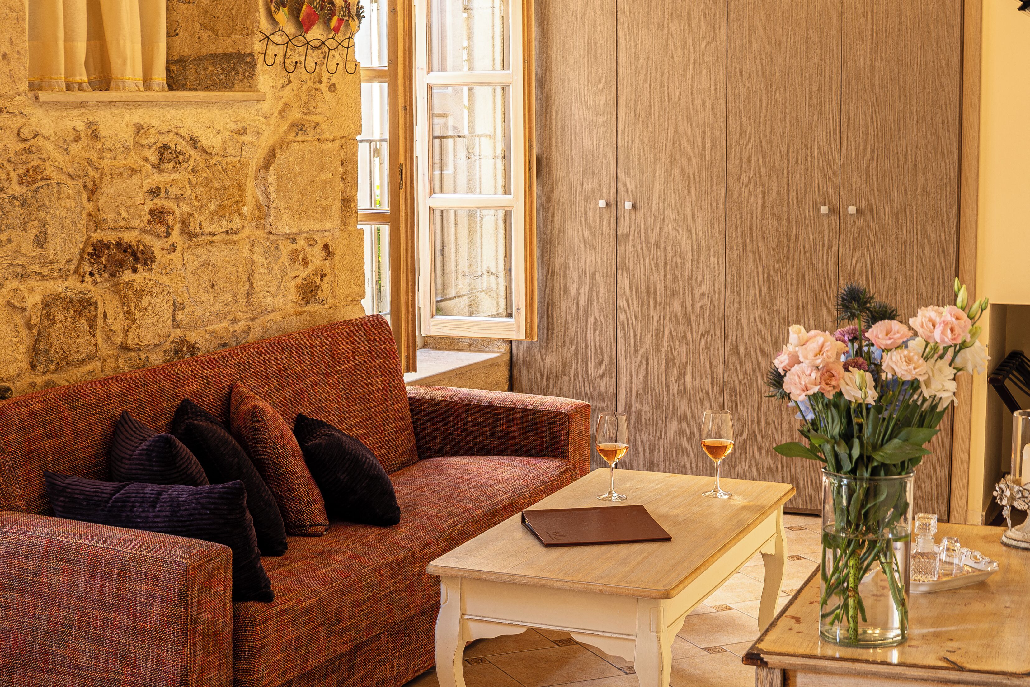 Una habitación acogedora con un sofá rojo, una mesa de madera, un jarrón de flores y una copa de vino.